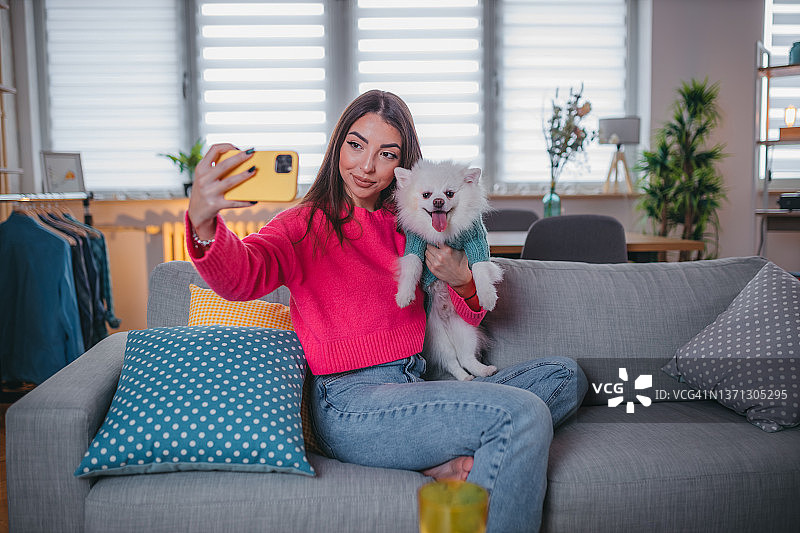 笑容满面的年轻女孩放松身心，抱着她的博美犬自拍图片素材