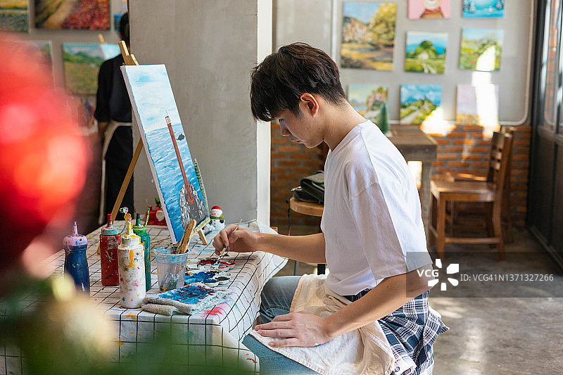 年轻的亚洲男子在家在画布上绘制丙烯颜料图片素材