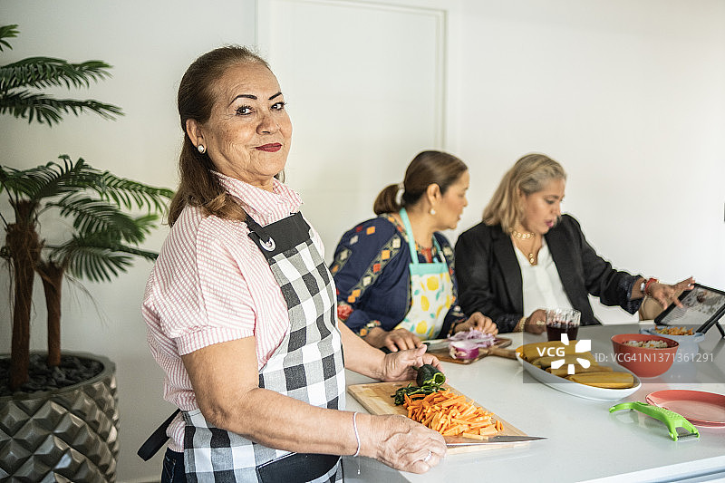 在家切胡萝卜的拉丁裔中年妇女肖像 - 准备墨西哥玉米粉蒸肉图片素材