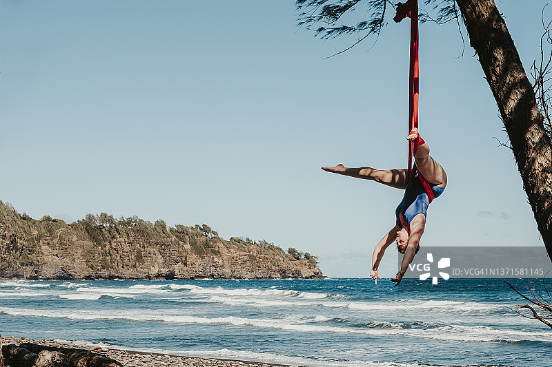 在夏威夷热带海滩上，女人在空中绸吊上倒挂表演图片素材