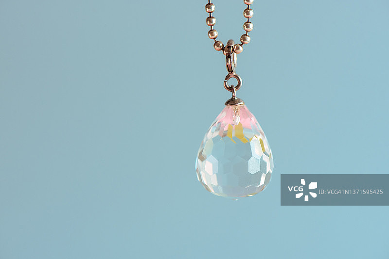 蓝色背景下，子弹头银链上水滴形状的水晶特写图片素材
