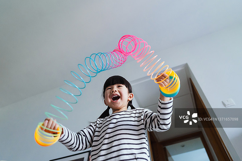 低角度拍摄的快乐亚洲小女孩在家玩彩色魔术弹簧彩虹玩具，简单的快乐和幸福，寓教于乐图片素材