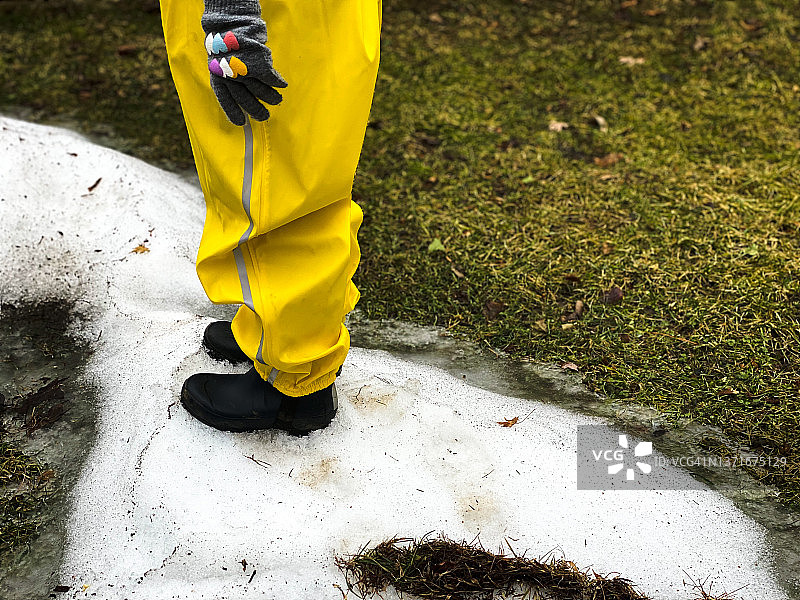 年轻女孩穿着亮黄色雨裤和橡胶靴，在外面玩耍最后的雪图片素材