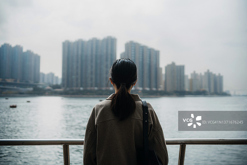 年轻的亚洲女子站在长廊旁，眺望着壮观的城市天际线的背影图片素材