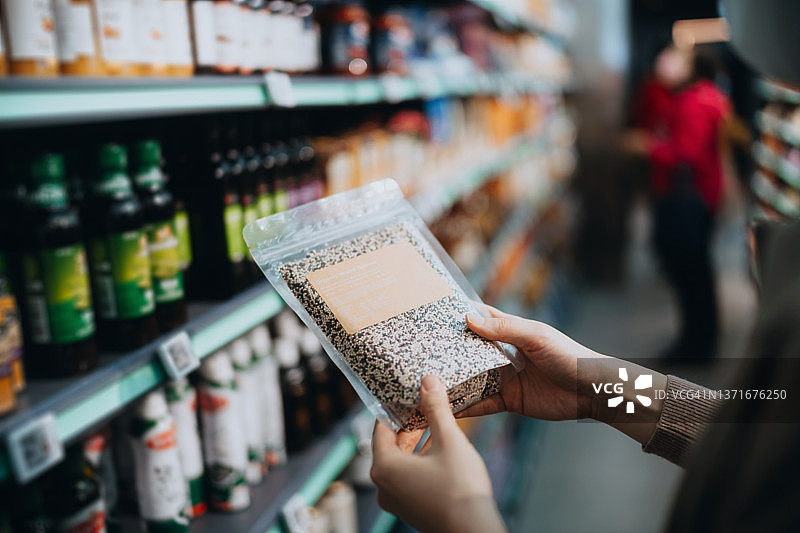 年轻亚裔女性在超市购买健康食品，查看藜麦营养成分图片素材