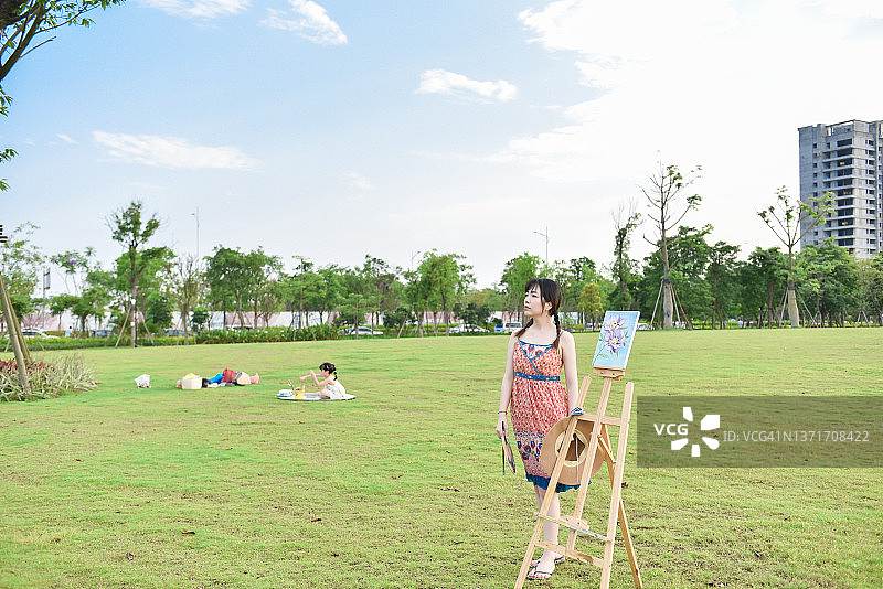 优雅的亚洲女画家（25-29岁）在公园沉思远望，女儿在她身旁玩耍，中国广东江门图片素材