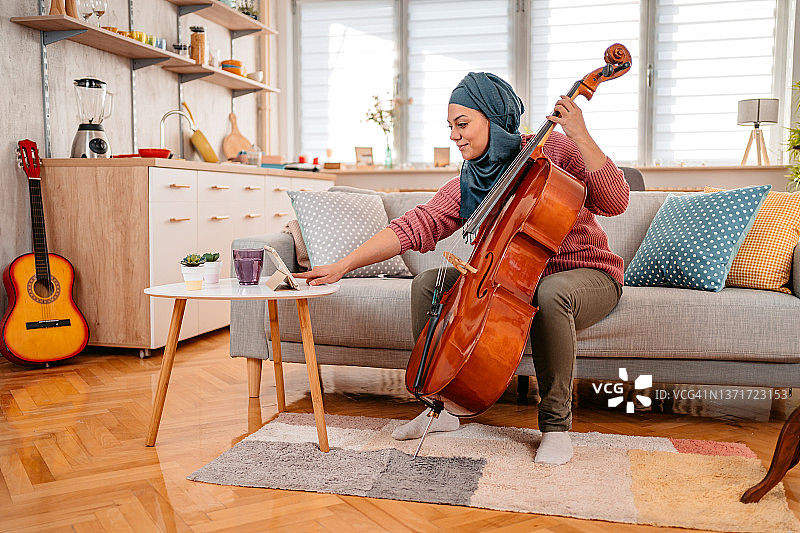 年轻穆斯林女性在平板电脑上看大提琴演奏教程图片素材