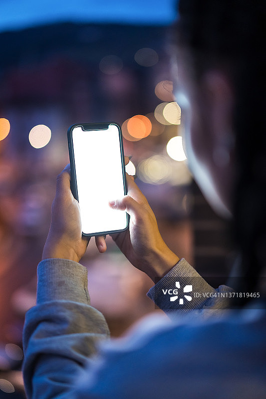 夜晚，拿着白色屏幕手机的无法辨认的女孩的手图片素材