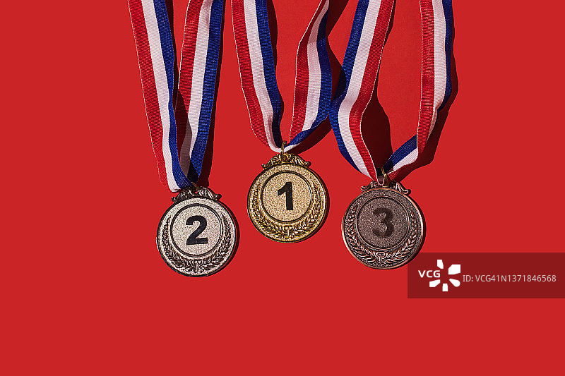红底上的金银铜体育奖牌，代表第一、二、三名。获胜者、奖牌、荣誉和体育竞赛概念图片素材