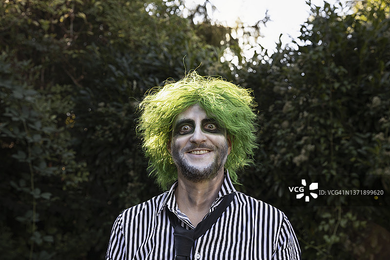 一位系着衬衫和领带、留着绿色波浪发型、化着万圣节彩绘、面部表情无忧无虑的年长成年人图片素材