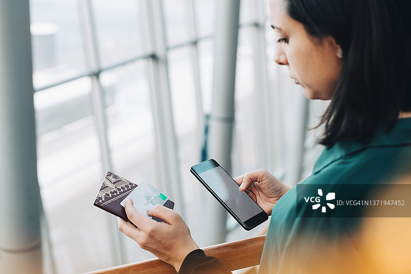 女商人拿着信用卡在机场使用手机（高角度）图片素材