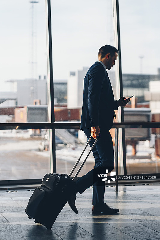 商务男士在机场行走时使用手机的侧面全身照图片素材