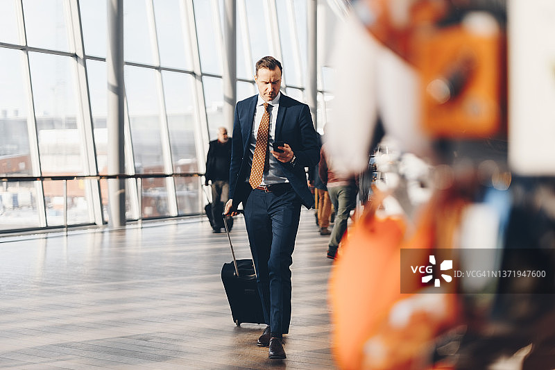成熟商人在机场航站楼拖着行李箱使用手机全身照图片素材
