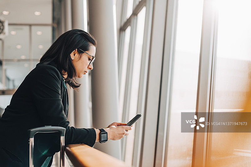 中年女商人靠在机场栏杆上使用手机的侧视图图片素材