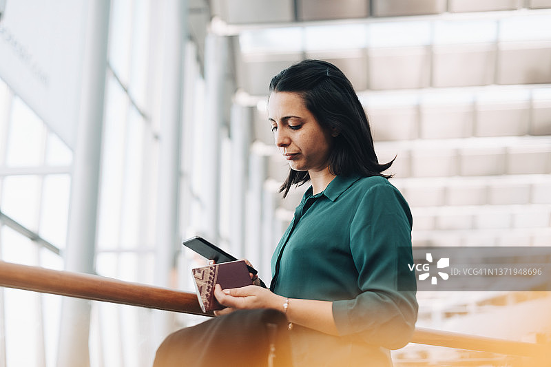 中年女商人在机场手持移动电话和护照图片素材