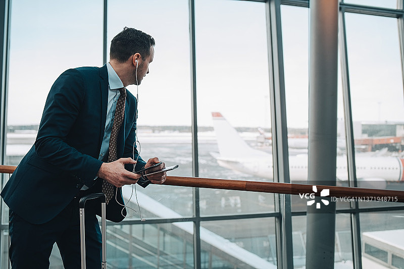 在机场用手机隔窗望飞机的商人图片素材