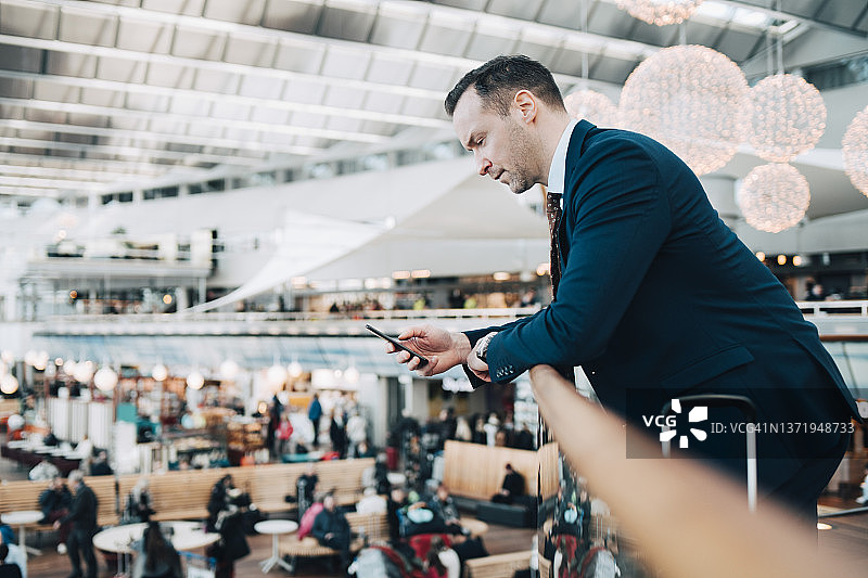 在机场栏杆旁使用手机的商务人士侧面照图片素材