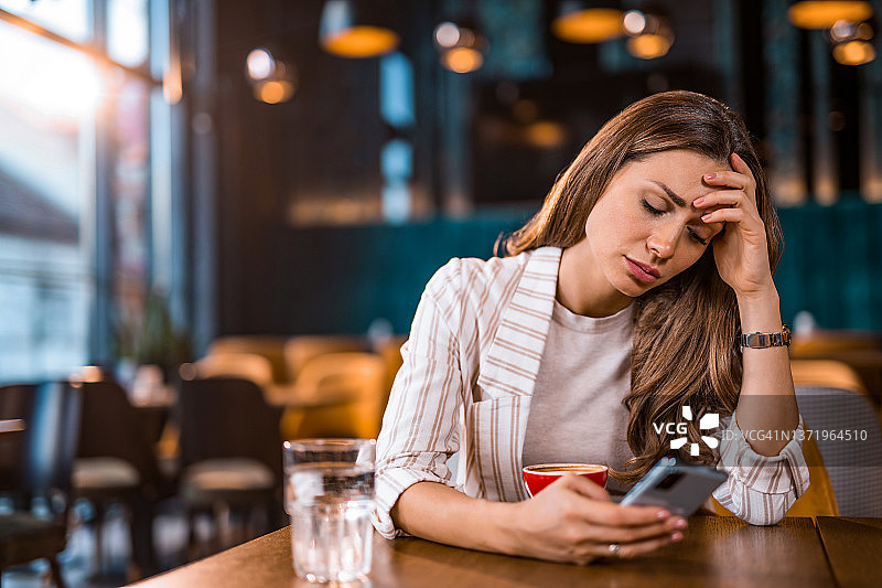 坐在咖啡馆里发短信的悲伤的年轻女人图片素材