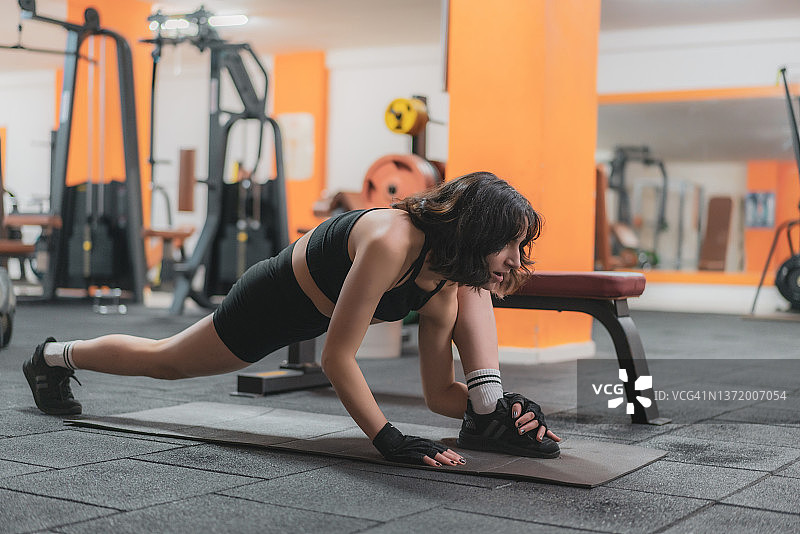 年轻女子在健身房的垫子上锻炼腹部肌肉图片素材