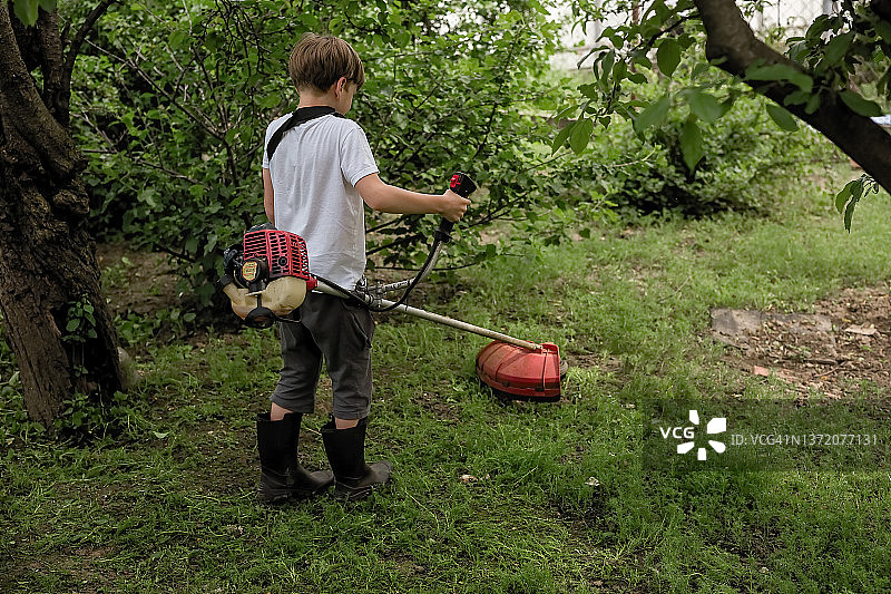 男孩用割草机修剪草坪。图片素材