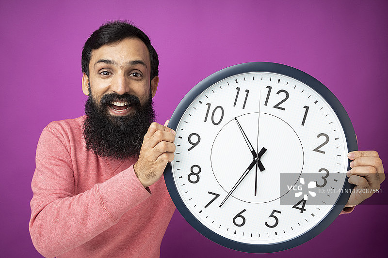 拿着时钟在紫色墙壁旁微笑的兴奋男子照片图片素材