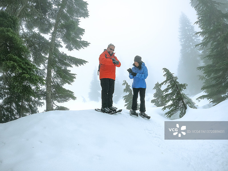 60多岁的多种族夫妇在雾气弥漫的森林里穿着雪鞋，整理袖子图片素材