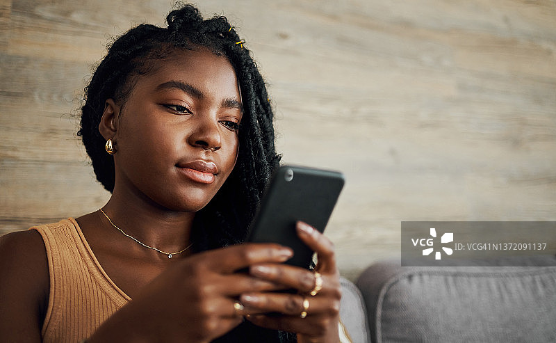 年轻有魅力的女人独自坐在客厅里，一边沉思一边使用手机图片素材