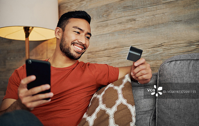 独自坐在客厅用手机网购的年轻男人照片图片素材