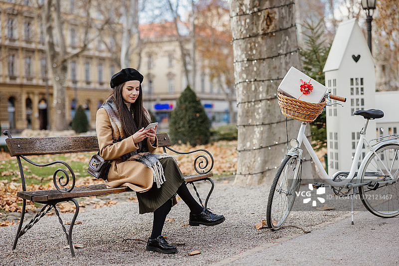 坐在公园长椅上使用手机的年轻女人图片素材