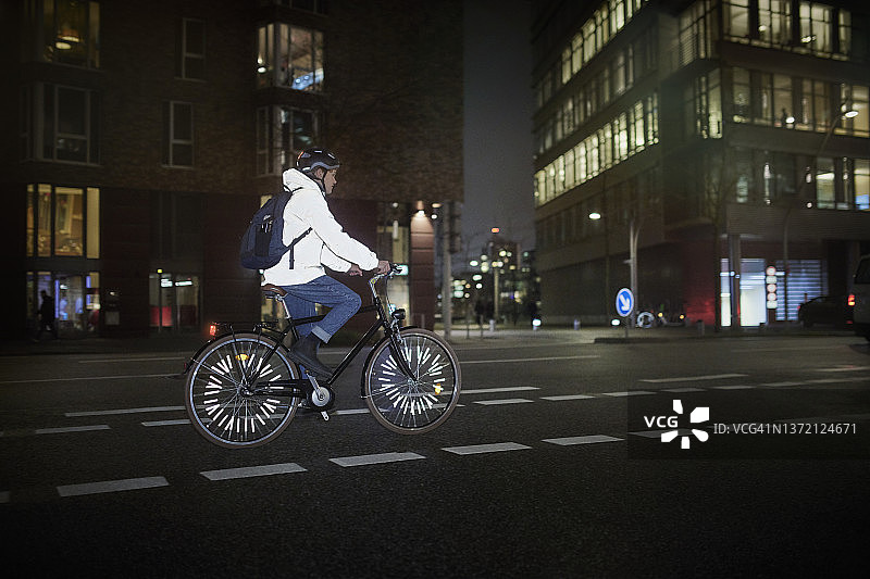 年轻男人夜晚在城市街道上骑自行车图片素材