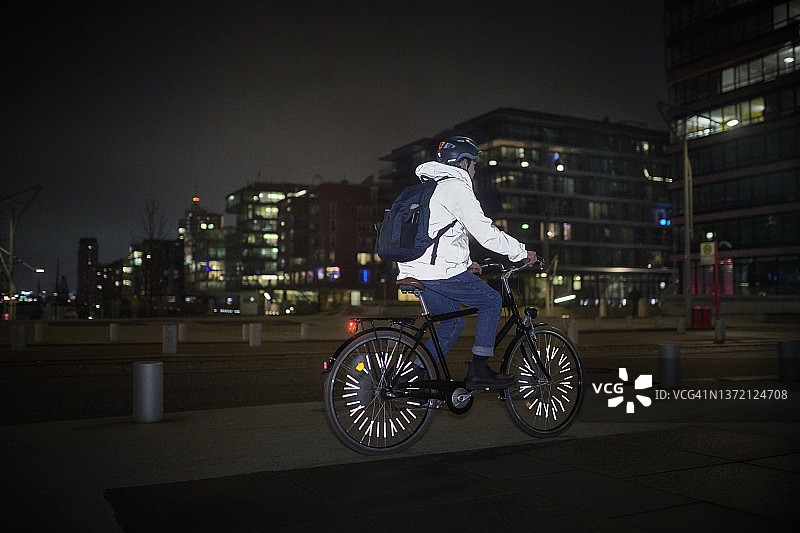 年轻男人夜晚在城市街道上骑自行车图片素材