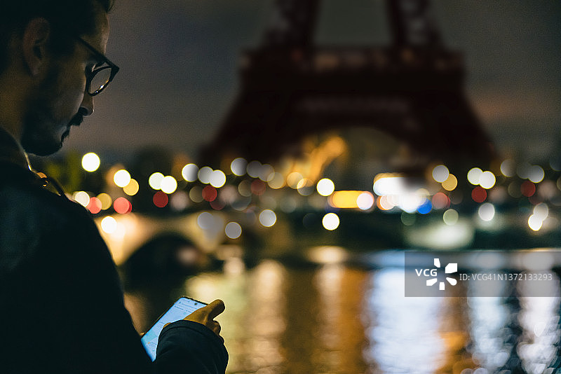 傍晚，男子在巴黎埃菲尔铁塔前看手机特写图片素材