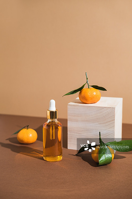 木制方台和棕色背景上的橙色精华液瓶，配有橘子。时尚风格。化妆品模型。留白。图片素材