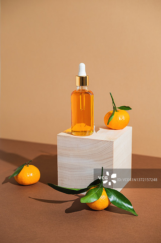 木制方台和棕色背景上的橙色精华液瓶，配有橘子。时尚风格。化妆品模型。留白。图片素材