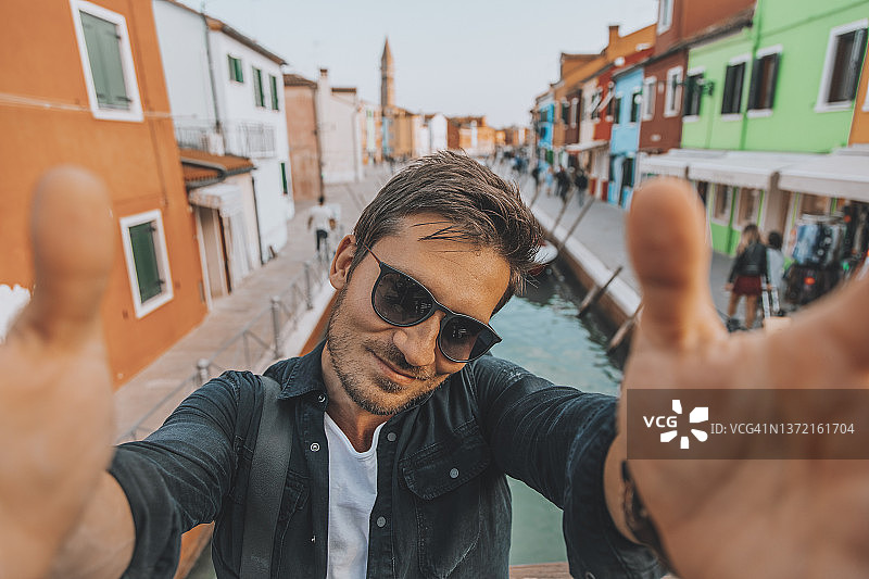 在意大利威尼斯布拉诺小镇用手机自拍的年轻人图片素材