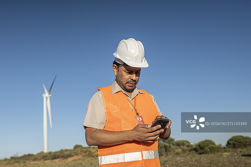 在风力发电场附近使用手机的电气工程师/技术员图片素材