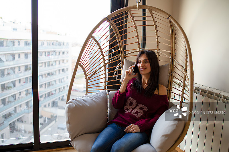 女人在悬挂椅上用手机讲话图片素材