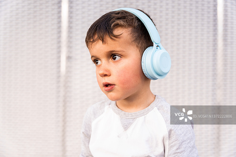 在白色纹理背景下，戴着无线耳机听音乐的六岁男孩图片素材