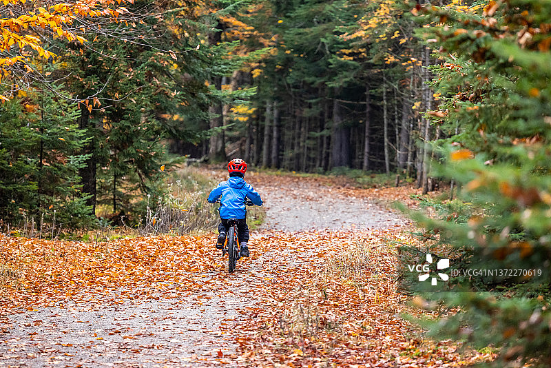 在加拿大魁北克省翠湖山国家公园秋季骑自行车的可爱红发男孩图片素材