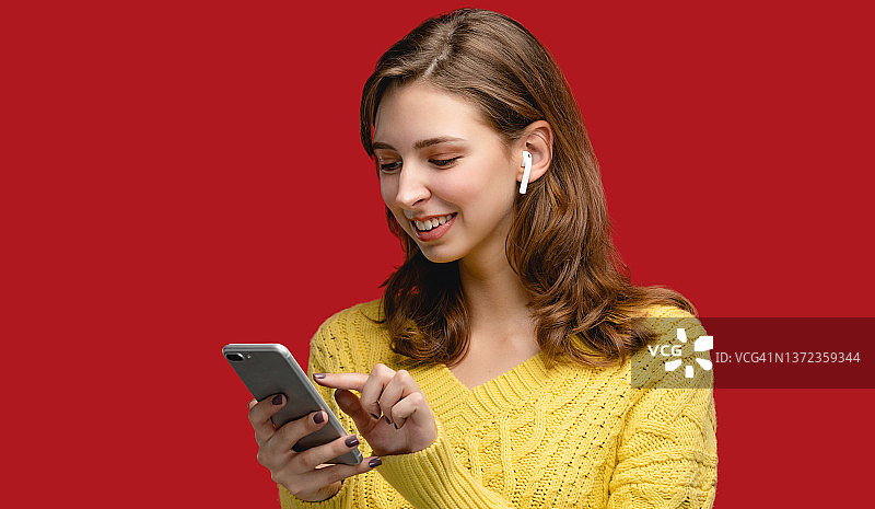 红色背景下使用手机和无线耳机工作的女子棚拍肖像图片素材