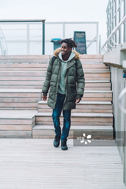 快乐的男人穿保暖衣物背背包街头木凳旁散步图片素材