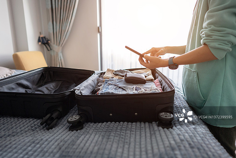 特写：青少年男孩在收拾行李箱准备公路旅行时使用手机图片素材
