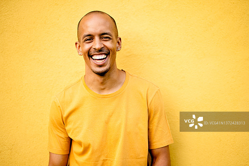 穿着黄色衬衫，在黄色墙边大笑的年轻人图片素材