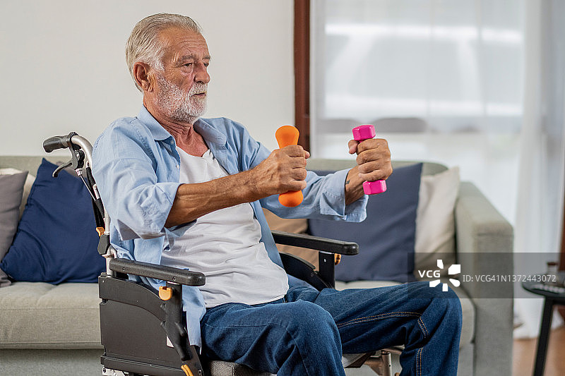 一位坐在轮椅上的年长男人在家用哑铃锻炼。图片素材
