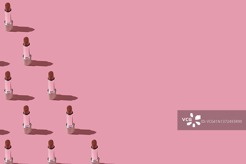 红色银管口红图案，硬阴影，位于粉色背景左侧。化妆、个人护理和性感概念图片素材