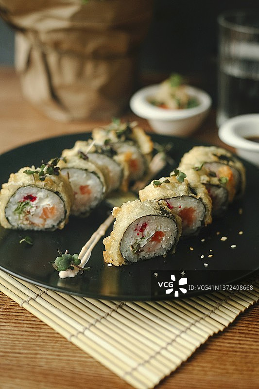 黑色餐盘中裹着天妇罗炸制的三文鱼寿司卷图片素材