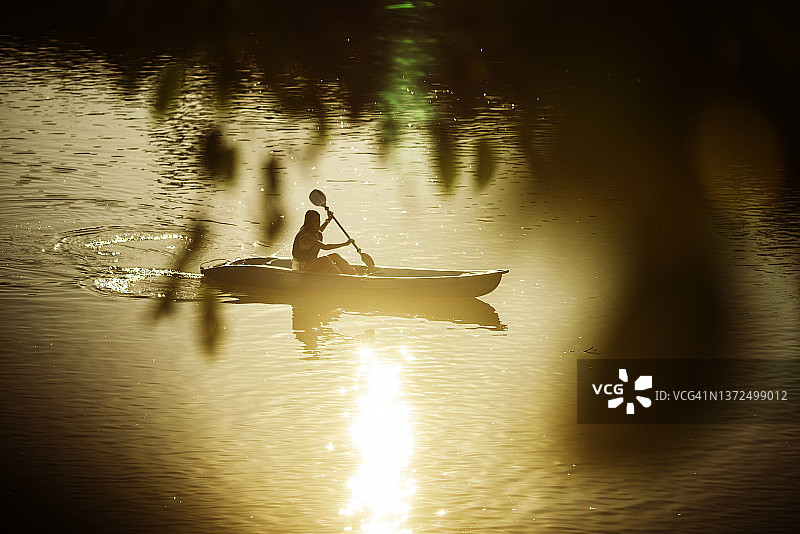 日落时分，亚洲青年在河中划皮划艇图片素材