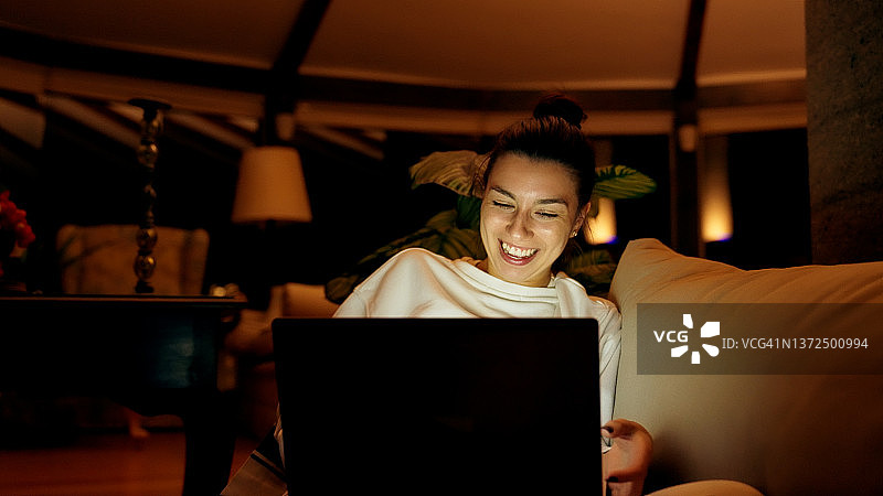 年轻女子在沙发上放松，用笔记本电脑观看有趣的电影图片素材