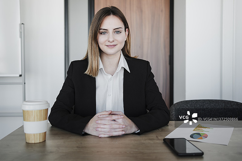 在办公室里双手合十坐在办公桌前的年轻女商人图片素材
