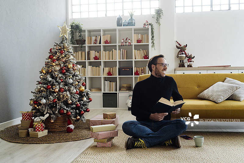 在家中圣诞树旁看书的男人图片素材